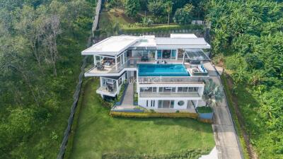Aerial view of a modern white multi-story house with a swimming pool, surrounded by greenery