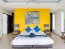 Modern bedroom with a yellow accent wall, double bed, and large painting
