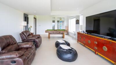 A spacious living room with leather recliners, bean bags, a large flat-screen TV, and a pool table.