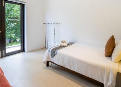 A minimalist bedroom with single bed, side table, and a large window with a view of greenery.