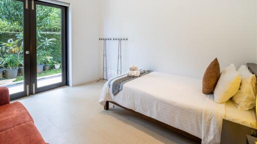 A minimalist bedroom with single bed, side table, and a large window with a view of greenery.