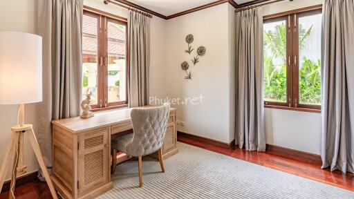 Bright and airy study room with wooden desk and chair, multiple windows, and wall decor.