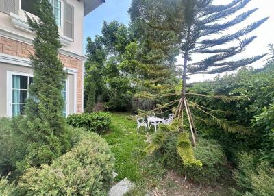 garden area with bushes, a small tree, a white round table, and three chairs