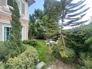 garden area with bushes, a small tree, a white round table, and three chairs