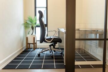 Modern home office with a large black chair, desk, and a plant in natural light