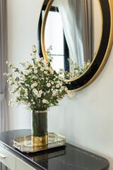 Decorative vase with flowers on a modern dresser, next to a round mirror