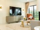 Modern living room with large TV, elegant furniture, and large windows