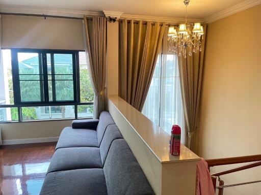 A cozy living room with a grey sofa, large window with curtains, and a chandelier lighting