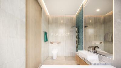 Modern bathroom with glass shower enclosure, toilet, green towel, wooden door, and large mirror