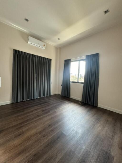 Empty bedroom with dark wood flooring, large windows with dark curtains, and a white air conditioning unit