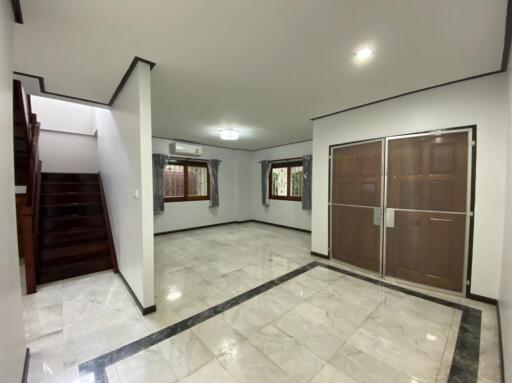 Spacious living room with marble flooring, large windows, and wooden staircase