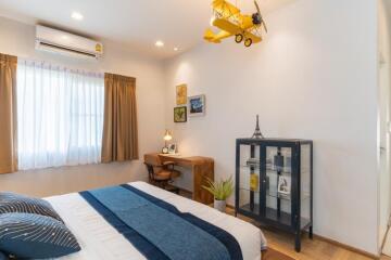 Cozy bedroom with a blue bedspread, wooden desk, window with curtains, and decorative items