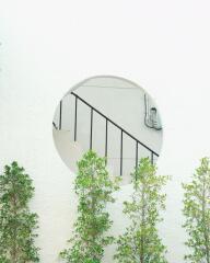 View of an architectural staircase through a round window with greenery in the foreground