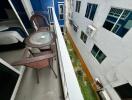 Balcony with wicker chairs and glass-top table overlooking neighboring building