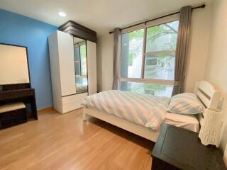 Bedroom with wooden flooring, blue accent wall, large window, bed, wardrobe, and dresser