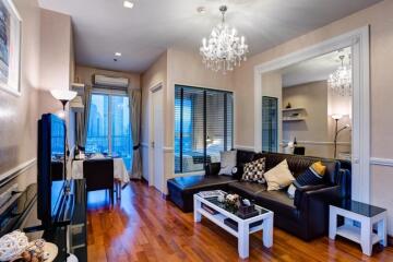 Modern living room with wooden flooring, chandelier, and glass windows