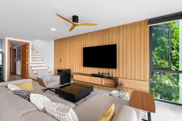 Modern living room with wooden panel wall, large TV, and natural light