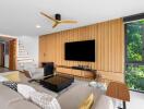 Modern living room with wooden panel wall, large TV, and natural light