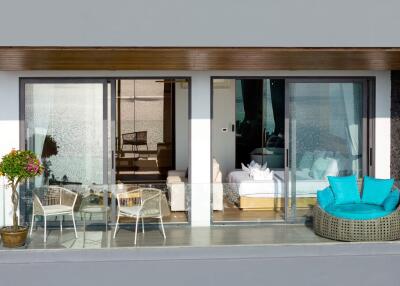 Balcony view of a modern apartment with outdoor seating and glass sliding doors leading to a living room and bedroom