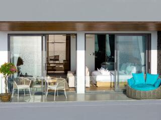 Balcony view of a modern apartment with outdoor seating and glass sliding doors leading to a living room and bedroom