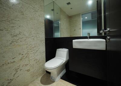 Modern bathroom with marble walls and flooring, featuring a toilet and a sink with a mirror