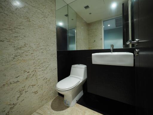 Modern bathroom with marble walls and flooring, featuring a toilet and a sink with a mirror