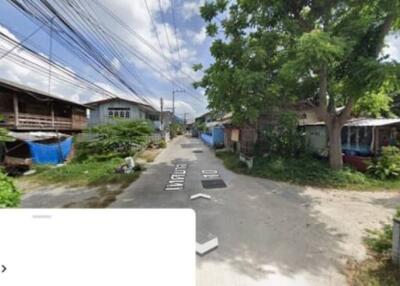 Street view of a residential neighborhood with houses, greenery, and overhead cables