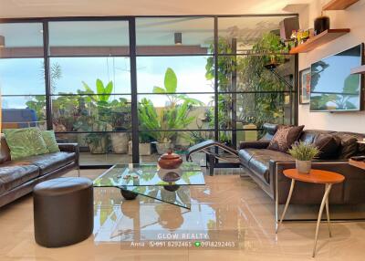 Spacious living room with glass coffee table, leather sofas, and large window overlooking greenery