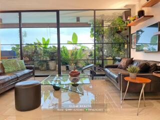 Spacious living room with glass coffee table, leather sofas, and large window overlooking greenery