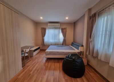 A cozy bedroom with wooden flooring, bed, and window drapes