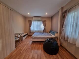 A cozy bedroom with wooden flooring, bed, and window drapes