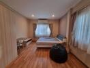 A cozy bedroom with wooden flooring, bed, and window drapes