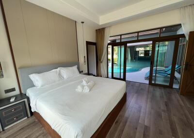 A spacious bedroom with a large bed, bedside tables, and a view of a pool through large glass doors
