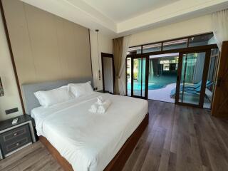 A spacious bedroom with a large bed, bedside tables, and a view of a pool through large glass doors