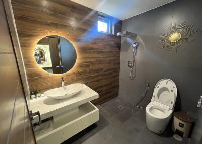 Modern bathroom with wooden and dark-colored tiles, featuring a round mirror, white sink, and a smart toilet.