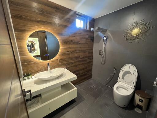 Modern bathroom with wooden and dark-colored tiles, featuring a round mirror, white sink, and a smart toilet.