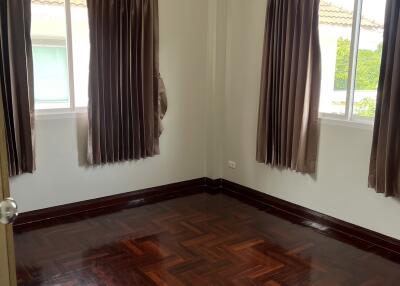 Empty bedroom with wooden flooring and windows with curtains