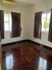 Empty bedroom with wooden flooring and windows with curtains