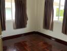 Empty bedroom with wooden flooring and windows with curtains