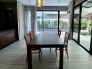 Modern dining room with wooden table and chairs, large windows, and garden view