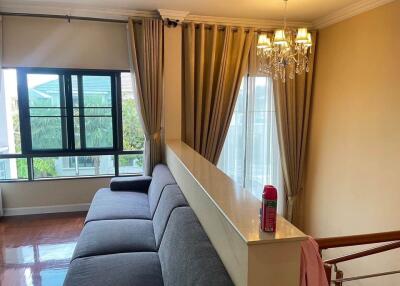 Living room with a large L-shaped sofa, two large windows with curtains, and a chandelier.