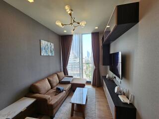 Modern living room with brown couch, coffee table, TV, and large windows