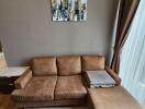 Brown sectional sofa in a living room with a painting hanging on a gray wall