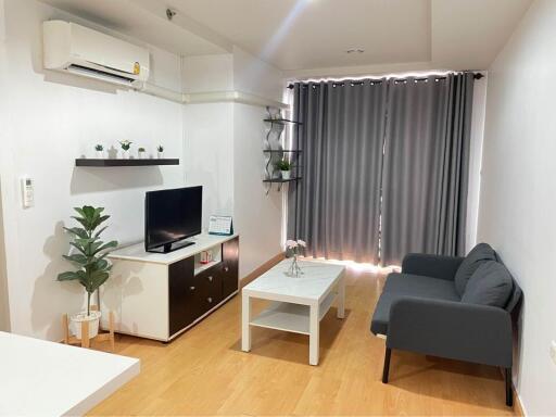 Modern living room with a sofa, coffee table, TV, potted plants, and wall-mounted air conditioner