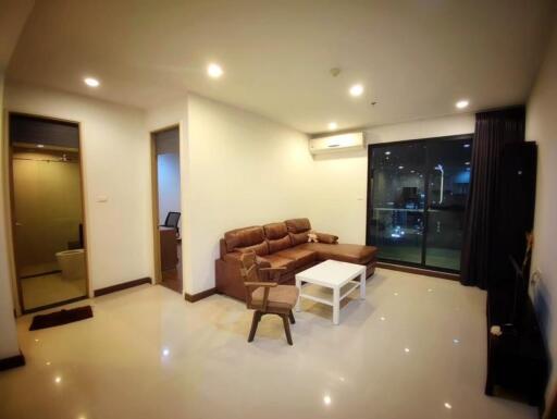 Spacious modern living room with brown leather sofas, white coffee table, and large sliding glass door to a balcony