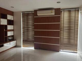 Living room with window blinds, wall air conditioner, and built-in shelves