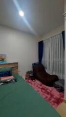 Bedroom with a green bedspread, brown lounge chair, books, and window with curtains