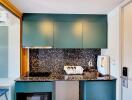 Compact modern kitchen with teal cabinets and black speckled countertop