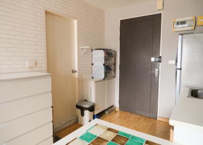 Small kitchen area with storage cabinets, refrigerator, and a door leading to another room