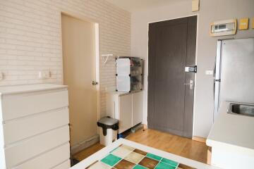 Small kitchen area with storage cabinets, refrigerator, and a door leading to another room